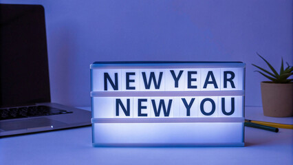 Fototapeta premium A calming blue-lit lightbox reads NEW YEAR NEW YOU, surrounded by a laptop, pencils, and a potted plant, evoking introspective vibes