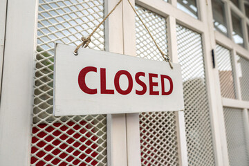 A white rectangular sign with CLOSED in bold red letters, hanging by strings against a white mesh background