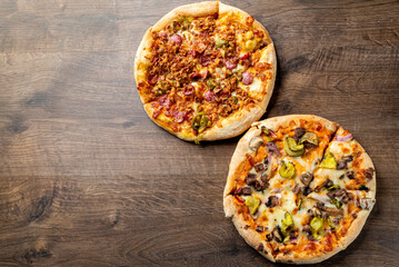 Two delicious pizzas on a wooden surface: one topped with pepperoni and vegetables, and the other featuring a mix of meats and peppers. Perfect for sharing or a tasty meal.