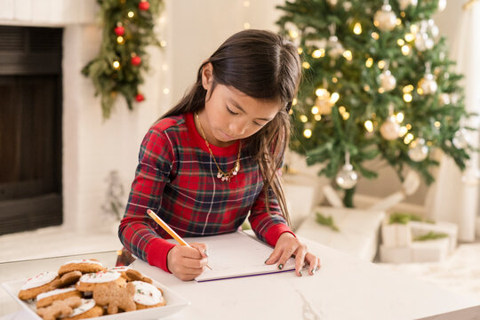 Girl writing to santa in front of christmas tree