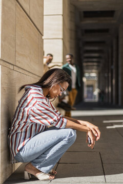 Young Latin woman squats down cause gets sad and frustrated outdoors