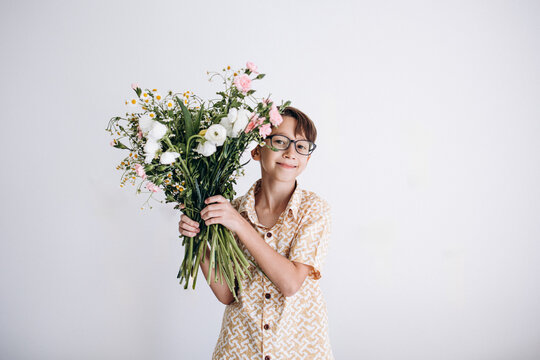 Boy holding large bouquet of flowers against white wall