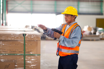 Warehouse staff working on barcode scanner handheld scanning a barcode on a box at warehouse factory.  senior Asian male warehouse worker or a supervisor.
