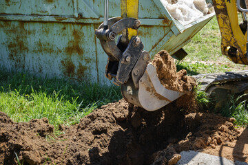 Mini excavator digs a narrow trench in soil for laying communications close-up. Mini bucket of...