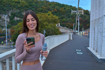 Sporty woman pausing on a city bridge, smiling happily while looking at her smartphone. Copy space