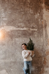 Obraz premium Mädchen steht mit kleinem Tannenbaum vor Betonwand