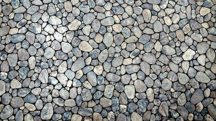 a surface covered with small, smooth pebbles. The pebbles vary in size and shape, with most being oval or round. They are tightly packed together, creating a mosaic-like pattern