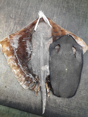 A dried ray fish, flat and wide, with its fins spread out, shows a smooth texture and light brown color.
