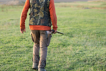 Mature hunter man holding a shotgun and walking through a field