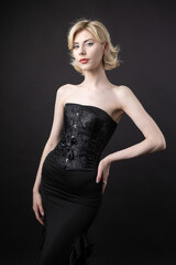 Expressive young blonde under a bob in the studio. In a black corset and dress.