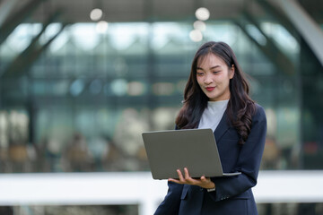 Asian independent woman, beautiful smiling student, doing business, studying Outdoors with laptop, interacting with customers on social media, studying online. Fashion concept, modern technology.