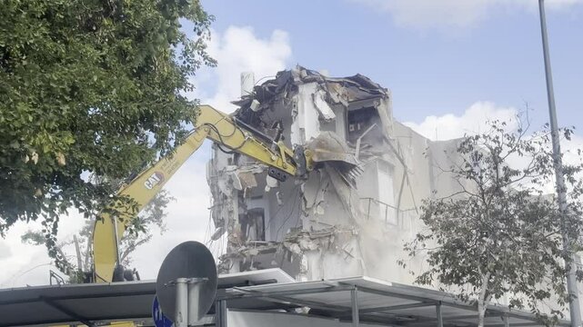 Excavator with large metal bucket breaks an old stone house. Demolition of obsolete building in city. Dangerous area is fenced off.