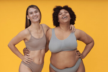 Portrait of happy body positive girls in underwear posing against yellow background