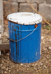 A blue bucket with a white lid sits on the ground