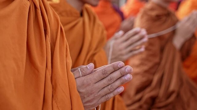 Pan shot of Buddhist monks hands praying while holding a holy thread during a religious event
