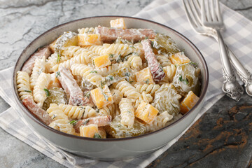 Creamy pickles pasta salad with yellow cheese, herbs and bacon close-up in bowl on table. Horizontal
