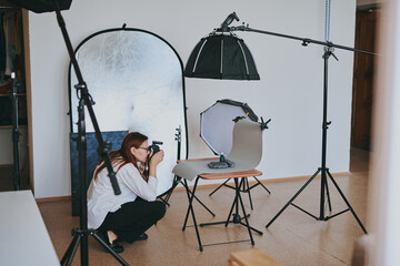 Female photographer taking photo of objects on background in photo studio with professional...