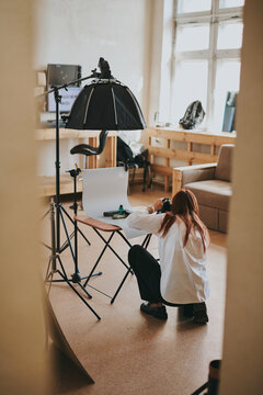 Female photographer taking photo of objects on background in photo studio with professional equipment
