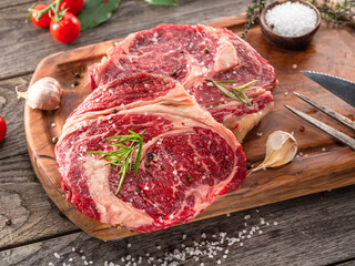 Raw beef steaks with herbs and spices ready for cooking are on wooden board.