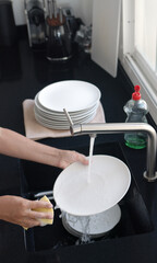 Washing and rinsing dishes by hand under a stream of water in the kitchen sink. Washing dishes process.