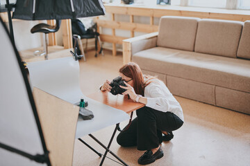 Female photographer taking photo of objects on background in photo studio with professional equipment