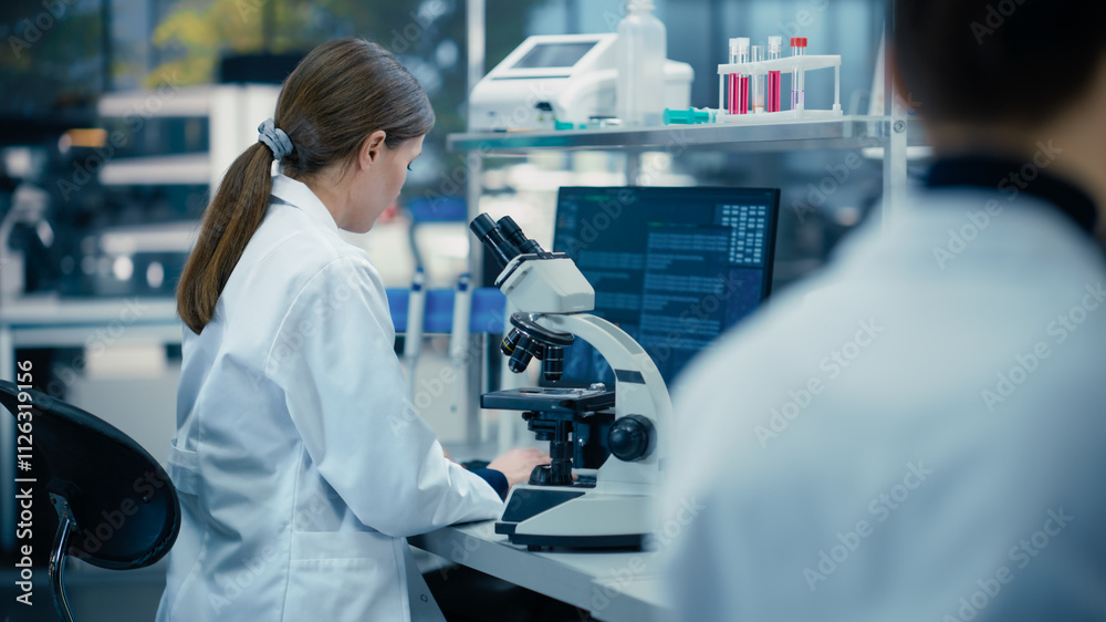 Leinwandbilder Medical Research Scientist Looking at Biological Samples Under a Microscope in an Applied Science Laboratory. Portrait of a Caucasian Lab Engineer in White Coat Sitting with Turned Back to Camera