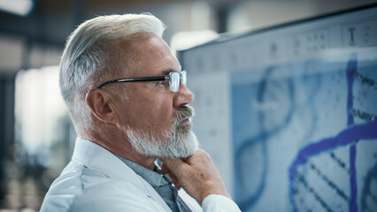 Senior Doctor in Glasses Examining a Scientific Experiment Report on a Big Screen. PhD Professor Looking at the Screen, Analyzing Provided Data and Technical Information. Biochemistry Concept