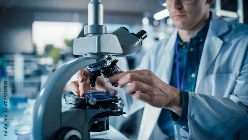 Poster close up portrait of a young microbiologist wearing glasses and looking through the microscope, anal