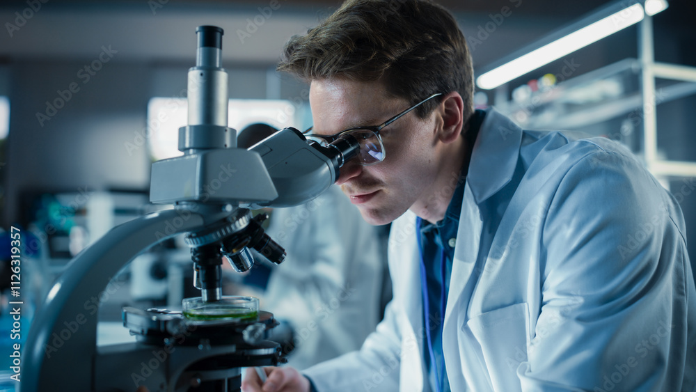 Poster Portrait of a Handsome Caucasian Student Working on a Research Project in University. Medical Research Scientist Looking at Biological Samples Under a Microscope in an Applied Science Laboratory