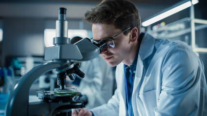 Portrait of a Handsome Caucasian Student Working on a Research Project in University. Medical Research Scientist Looking at Biological Samples Under a Microscope in an Applied Science Laboratory