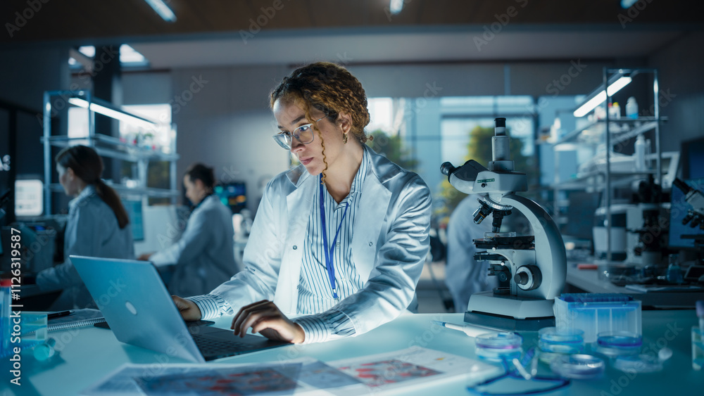 Leinwandbilder Beautiful Multiethnic Female Scientist Working on a Computer and Looking at a Sample in a Petri Dish Under a Microscope. Specialists Working in an Advanced Medical Research and Development Laboratory