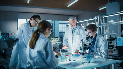 Obraz premium Young Team of Science Researchers Sitting Behind a Table, Using Microscopes for Medical Pharmaceutical Research and Treatment Development. Senior Scientist Supervising the Project