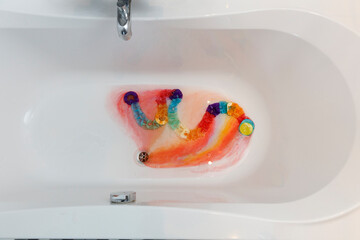 Rainbow gummy candies in a bathtub, creating a colorful mess.  Water and bubbles surround the...