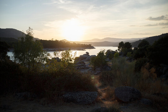 Sunset over a serene lake nestled in a valley.  Rocky shoreline, trees, and hills frame the tranquil scene.