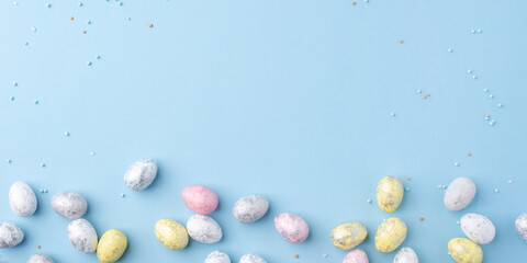 Festive Easter background. Multicolored Easter eggs on a blue table. Banner with a place for text. Top view.