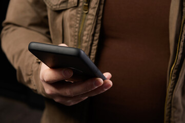 Mature man with small belly holds his smartphone in one hand while replying to message or surfing internet