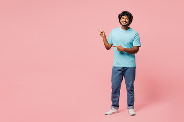Full body young smiling happy Indian man he wear blue t-shirt casual clothes point index finger aside on area mock up isolated on plain pastel light pink background studio portrait. Lifestyle concept.