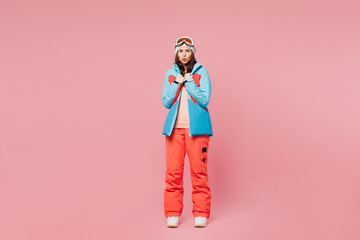 Full body skier sad young freezing woman wears blue padded jacket ski goggles mask spend weekend winter season in mountains warm herself look camera isolated on plain pink background. Hobby concept.