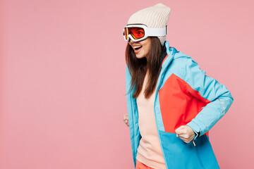 Side profile view skier young woman wear blue padded jacket ski goggles mask spend extreme weekend winter season in mountains walk go pov hold poles isolated on plain pink background. Hobby concept. © ViDi Studio