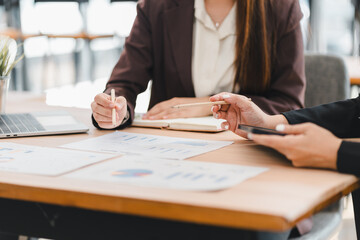 Two business professionals discussing financial charts and data at wooden desk, with laptop and smartphone in use, showcasing teamwork and collaboration in modern office
