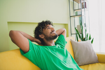 Photo of handsome young guy relax sit couch hands behind head dressed green garment spacious house...