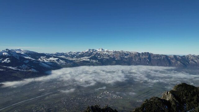 Aerial shot flying sideway with a stunning view over the rhein valley during a sunny autumn day. Some fog in the vally but perfect weather on the Alpstein in the background.