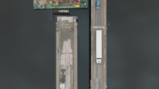 Aerial top down bridge construction process, machinery, traffic over Salacgriva city Salaca river, wide birdseye dolly shot
