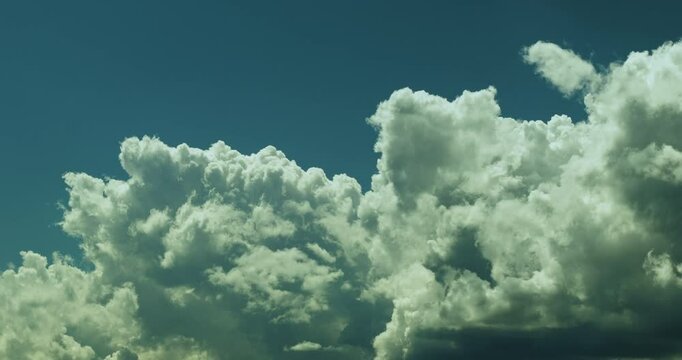 Timelapse of a detail of spectacular huge and fluffy white and grey cumulus cloud gathering for a storm and billowing and swelling on the background of the clear blue sky