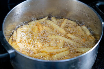 Potatoes in boiling oil, homemade french fries, deep fried potato cooking in metal fryer pot, fat fast food
