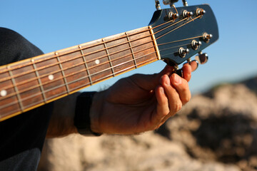 Close-up of a man tuning an acoustic guitar outdoors

