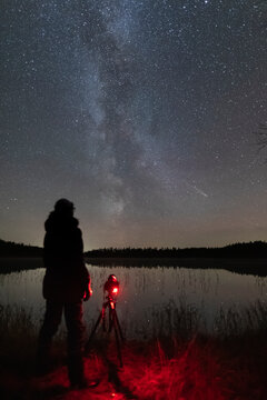 A person takes a photo of the night sky showing the Milky Way and a comet