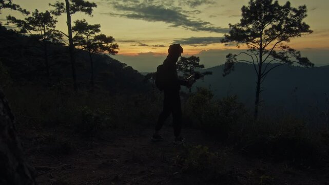 A young man holds a microphone to record his surroundings against the backdrop of a mountain sunset