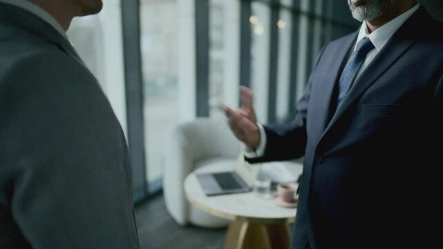 Senior businessman with grey beard, wearing formal suit, giving handshake and talking to colleague. Midsection, close-up shot