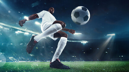 Low angle view on focused man, soccer player in white uniform, dribbling ball with precision against evening sky and fans tribune on background. Concept of sport, tournament, competition, game event